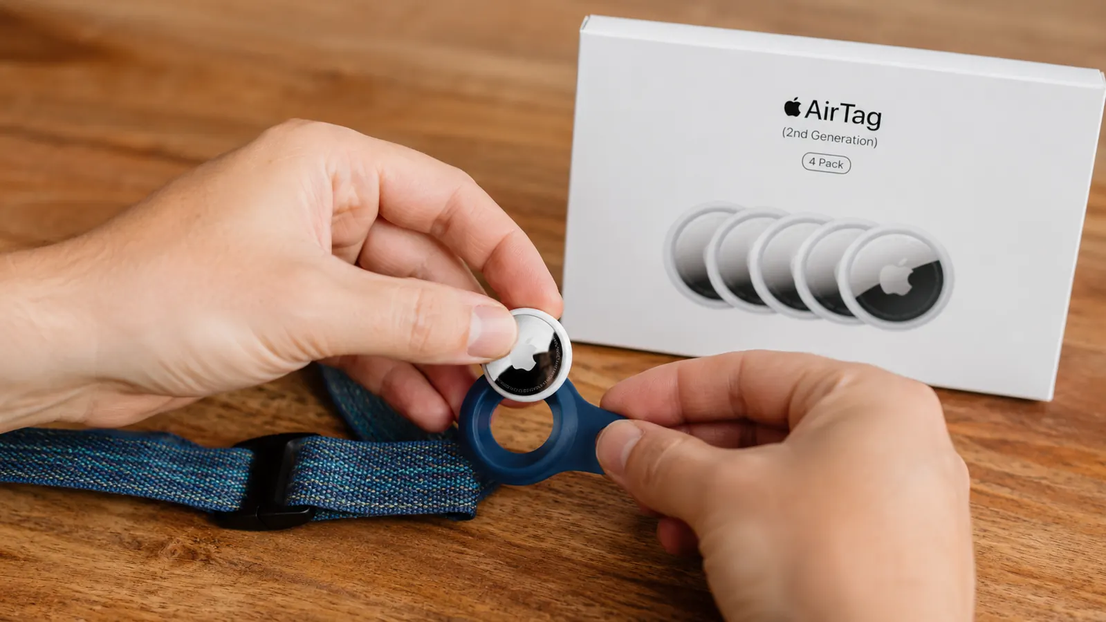 Hand holding an Apple AirTag next to a dog collar loop attachment on a wooden table